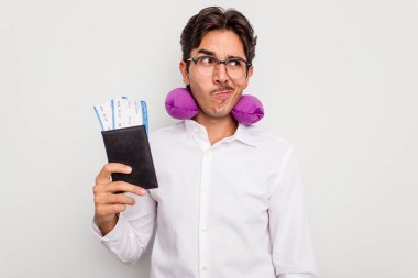 Beyaz arka planda izole edilmiş pasaport taşıyan şişme yastıklı genç İspanyol adam şaşkın ve kararsız hissediyor..