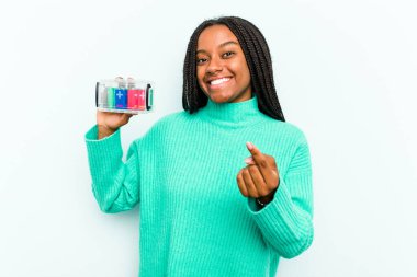 Genç Afrikalı Amerikalı bir kadın elinde batarya kutusuyla mavi arka planda izole bir şekilde seni işaret ediyor sanki davet ediyormuş gibi..