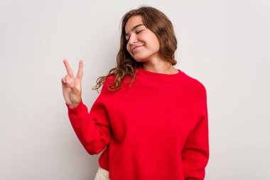 Mavi arka planda izole edilmiş genç beyaz kadın neşeli ve kaygısız parmakları olan bir barış sembolü gösteriyor..