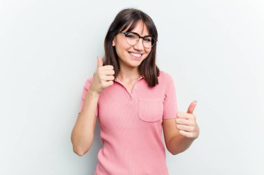 Beyaz arka planda soyutlanmış beyaz tenli genç bir kadın iki parmağını da kaldırıyor, gülümsüyor ve kendinden emin..