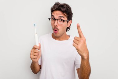 Beyaz arka planda elektrikli diş fırçası tutan İspanyol genç adamın bir fikri var, ilham verici bir kavram..