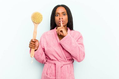 Genç Afrikalı Amerikalı bir kadın elinde küvet fırçası ile mavi arka planda izole edilmiş bir şekilde bir sır saklıyor ya da sessizlik istiyor..