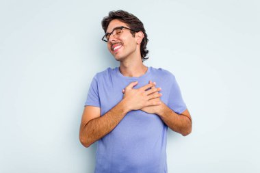 Mavi arka planda izole edilmiş genç İspanyol adam, avuçlarını göğsüne bastıran dostça bir ifadeye sahiptir. Aşk konsepti.