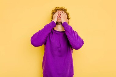 Sarı arka planda izole edilmiş genç beyaz adam ellerini başının üstünde tutarak neşe içinde gülüyor. Mutluluk kavramı.