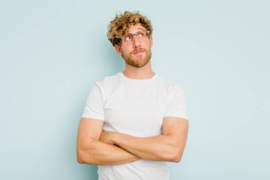 Kafkasyalı genç adam mavi arka planda izole edilmiş hedeflerine ve amaçlarına ulaşma hayali kuruyor.