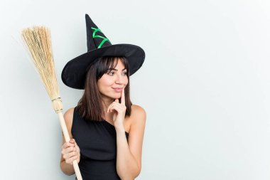 Cadı gibi giyinmiş beyaz bir kadın elinde süpürgeyle mavi arka planda izole edilmiş bir şekilde duruyor. Bir şeyin fotokopi odasına baktığını düşünerek rahatlıyor..