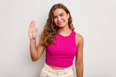 Mavi arka planda izole edilmiş genç beyaz kadın gülümseyerek beş numarayı parmaklarıyla gösteriyor..
