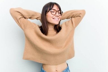 Beyaz arka planda soyutlanmış beyaz tenli genç bir kadın kendini güvende hissediyor, elleri başının arkasında..