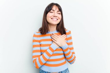 Beyaz arka planda soyutlanmış beyaz tenli genç bir kadın gülüyor, ellerini kalbe koyuyor, mutluluk kavramını koruyor..