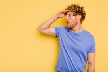 Kafkasyalı genç adam sarı arka planda izole edilmiş, uzaklara bakıyor ve elini alnına koyuyor..