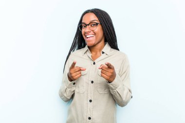Saçları mavi arka planda izole edilmiş, parmaklarıyla öne bakan genç Afrikalı Amerikalı kadın..