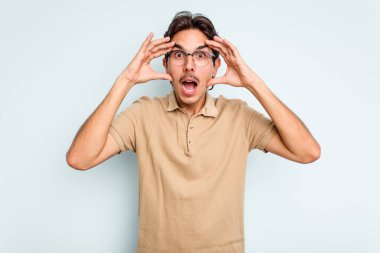 Genç İspanyol bir adam mavi arka planda izole edilmiş. Hoş bir sürpriz bekliyor. Heyecanlı ve el kaldırıyor..