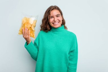 Mavi arka planda patates cipsi tutan beyaz bir kadın. Mutlu, güler yüzlü ve neşeli..