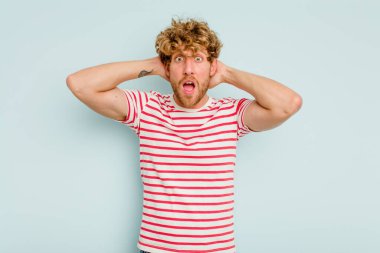 Genç beyaz adam mavi arka planda izole edilmiş bağırıyor, çok heyecanlı, tutkulu, bir şeyden memnun..