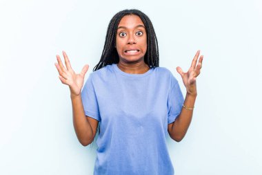 Saçları örgülü genç Afrikalı bir kadın mavi arka planda izole edilmiş, gökyüzüne haykırıyor, yukarı bakıyor, hayal kırıklığına uğramış..