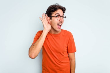 Genç İspanyol bir adam mavi arka planda izole edilmiş bir şekilde bir dedikoduyu dinlemeye çalışıyor..