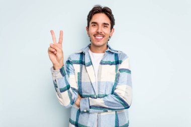 Mavi arka planda izole edilmiş genç İspanyol adam iki numarayı parmaklarıyla gösteriyor..