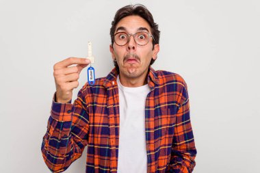 Beyaz arka planda izole edilmiş ev anahtarlarını tutan İspanyol genç adam omuz silkiyor ve gözleri açık..