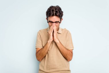 Genç İspanyol adam mavi arka planda izole edilmiş dua ediyor, bağlılık gösteriyor, dindar biri ilahi ilhamı arıyor..