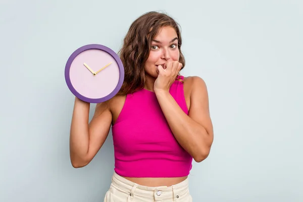 Mujer Caucásica Joven Sosteniendo Reloj Aislado Sobre Fondo Azul Mordiendo —  Fotos de Stock