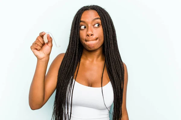 Ung Afroamerikansk Kvinna Som Håller Hörapparaten Isolerad Blå Bakgrund Förvirrad — Stockfoto