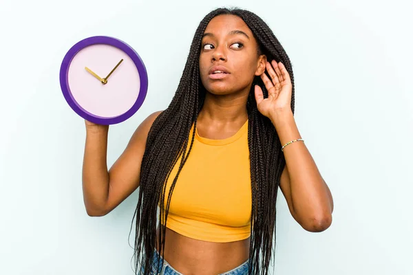 Молодая Афроамериканка Держащая Часы Голубом Фоне Пытается Слушать Сплетни — стоковое фото
