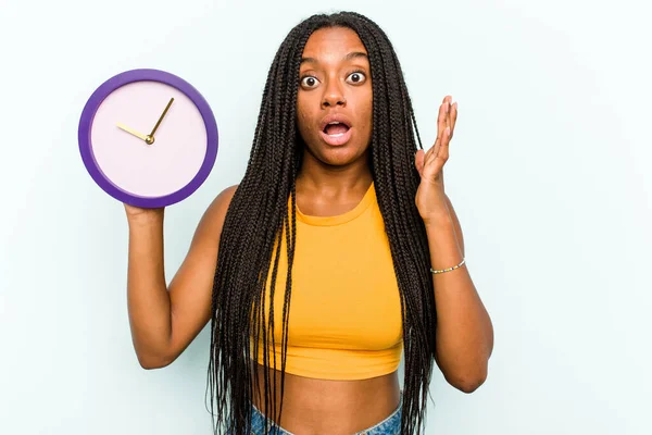 Молодая Афроамериканка Держащая Часы Голубом Фоне Удивлена Шокирована — стоковое фото