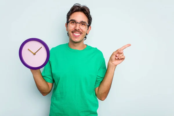 Jovem Hispânico Segurando Relógio Isolado Fundo Branco Sorrindo Apontando Para — Fotografia de Stock