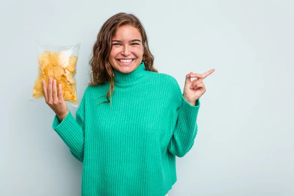 Jovem Caucasiana Segurando Batatas Fritas Isoladas Fundo Azul Sorrindo Apontando — Fotografia de Stock