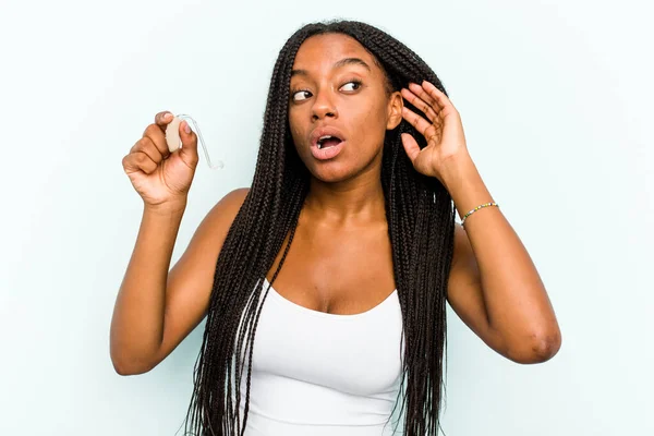 Молодая Афроамериканка Держащая Слуховой Аппарат Синем Фоне Пытается Слушать Сплетни — стоковое фото