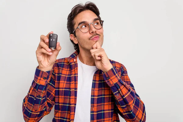 Young hispanic man holding car keys isolated on white background looking sideways with doubtful and skeptical expression.
