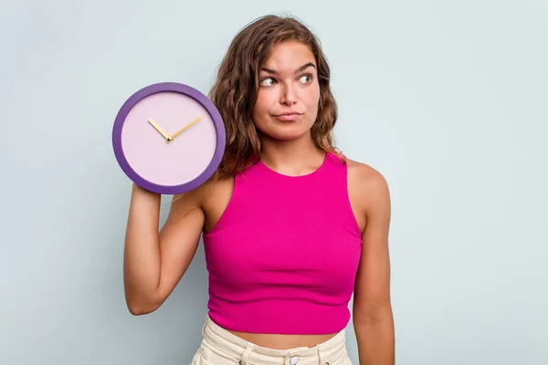 Mujer Caucásica Joven Sosteniendo Reloj Aislado Sobre Fondo Azul Confundido —  Fotos de Stock