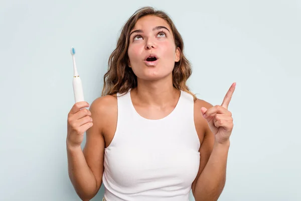 若いですCaucasian女性を持っています電動歯ブラシ隔離された青の背景上を指すとともにオープン口 — ストック写真