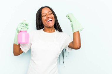 Genç Afrikalı Amerikalı temizlikçi kadın mavi arka planda izole edilmiş zafer kazandıktan sonra yumruğunu kaldırıyor, kazanan konsept.