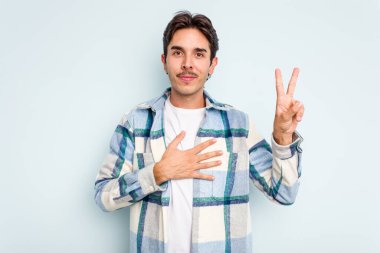 Genç İspanyol bir adam mavi arka planda izole edilmiş yemin ediyor, elini göğsüne koyuyor..