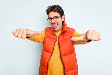 Genç İspanyol adam mavi arka planda izole edilmiş. Baş parmağını kaldırıyor, gülümsüyor ve kendinden emin..