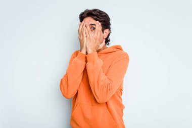 Genç İspanyol adam mavi arka planda izole edilmiş. Korkmuş ve gergin parmaklarıyla göz kırp..