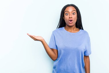 Mavi arka planda saç örgüsü olan genç Afrikalı Amerikalı kadın avuç içi fotokopi alanını tutmaktan etkilenmiş..