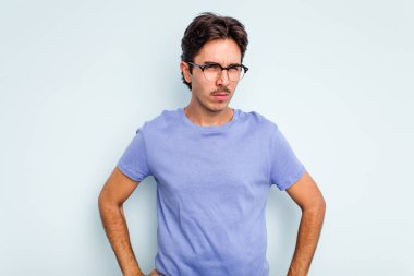 Mavi arka planda izole edilmiş, hoşnutsuzca kaşlarını çatmış, kollarını kavuşturmuş genç bir İspanyol..