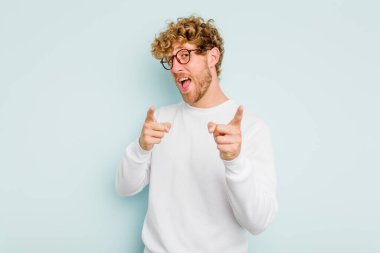 Mavi arka planda izole edilmiş genç beyaz adam parmaklarıyla ön tarafı işaret ediyor..