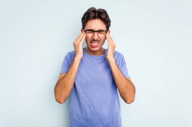 Genç İspanyol adam mavi arka planda izole edilmiş tapınaklara dokunuyor ve baş ağrısı çekiyor..