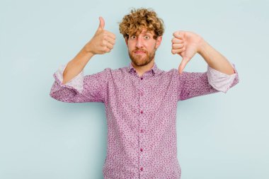 Kafkasyalı genç adam mavi arka planda izole edilmiş, baş parmağını kaldırıyor, zor seçim konsepti.