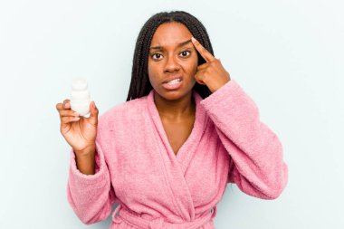 Bornoz giyen genç Afrikalı bir kadın mavi arka planda izole edilmiş bir deodorant tutuyor işaret parmağıyla yaptığı hayal kırıklığı jestini gösteriyor..