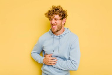Sarı arka planda karaciğer ağrısı çeken, karnı ağrıyan genç beyaz bir adam..