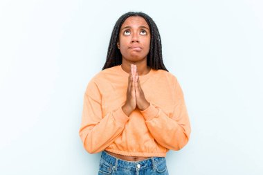 Saçları mavi arka planda izole edilmiş, ağzı yakınında dua eden genç Afrikalı Amerikalı kadın kendini güvende hissediyor..