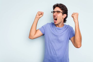 Mavi arka planda izole edilmiş genç İspanyol bir adam zaferden sonra yumruk kaldırıyor, kazanan konsept..