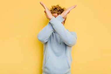 Sarı arka planda izole genç beyaz adam iki kolu çapraz tutuyor, inkar kavramı.