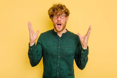 Sarı arka planda izole edilmiş genç beyaz adam gökyüzüne haykırıyor, yukarı bakıyor, hayal kırıklığına uğramış..