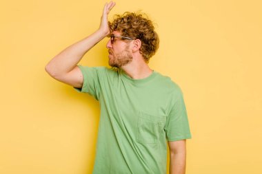 Sarı arka planda izole edilmiş genç beyaz bir adam bir şeyi unutuyor. Alnına avuç içi ve gözlerini kapayarak vuruyor..