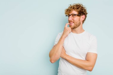 Mavi arka planda izole edilmiş genç beyaz adam rahatlamış bir şeyin fotokopi odasına baktığını düşünüyor..